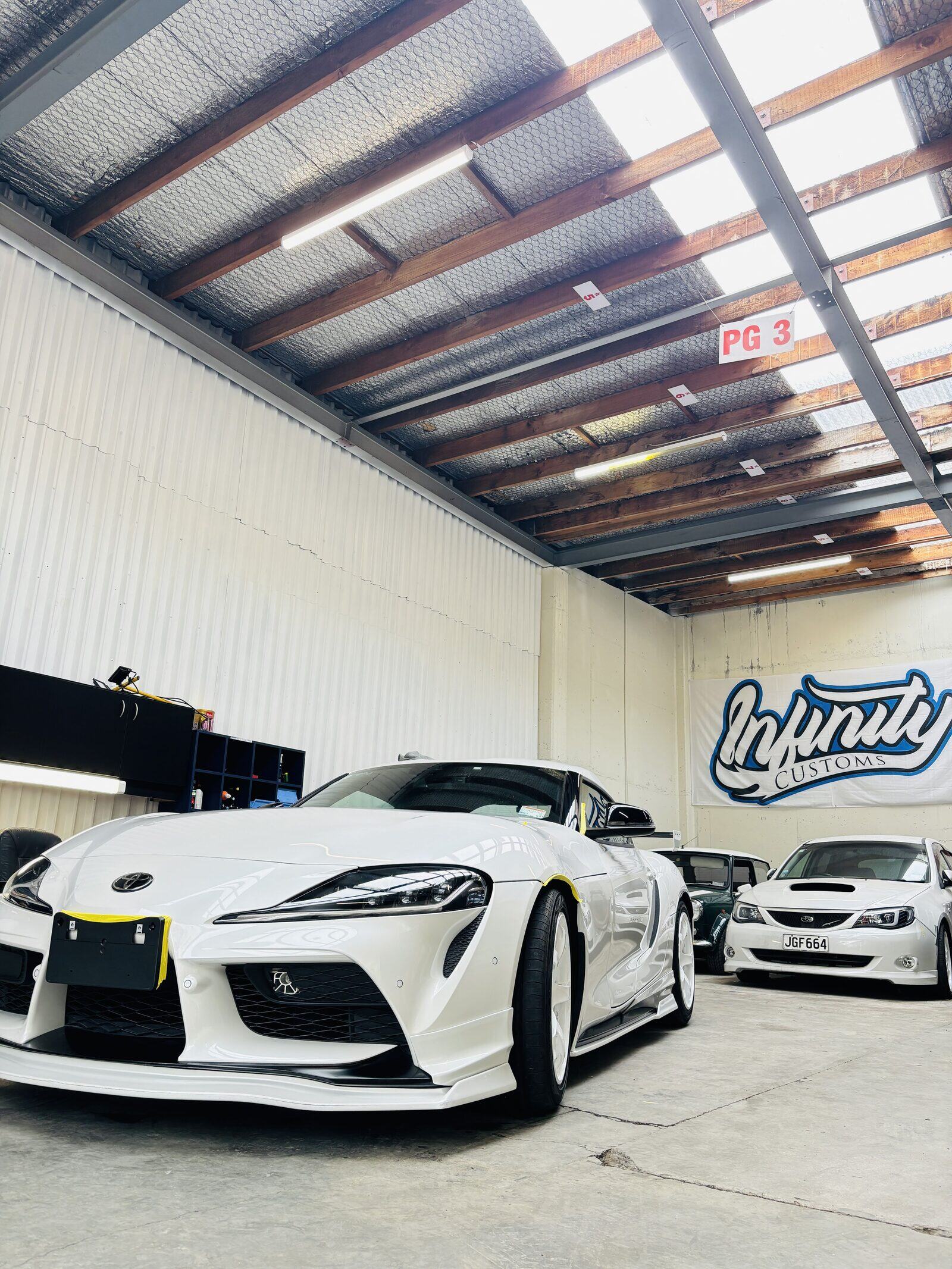A white Toyota Supra parked inside our Taita workshop under the Infinity Customs banner